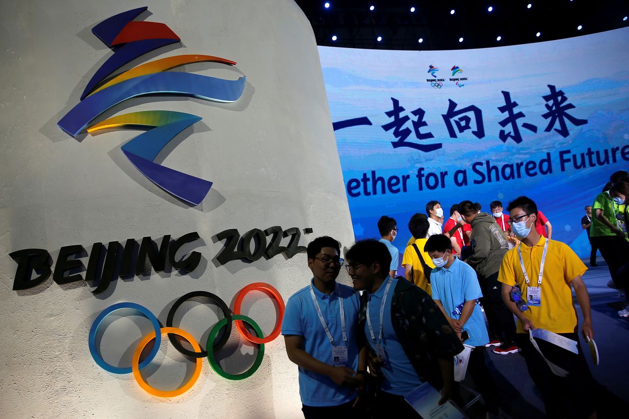 FILE PHOTO: Attendees walk past an emblem of the Beijing 2022 Winter Olympic Games next to a screen showing the slogan, "Together for a shared future", following a ceremony in Beijing, China September 17, 2021. REUTERS/Tingshu Wang