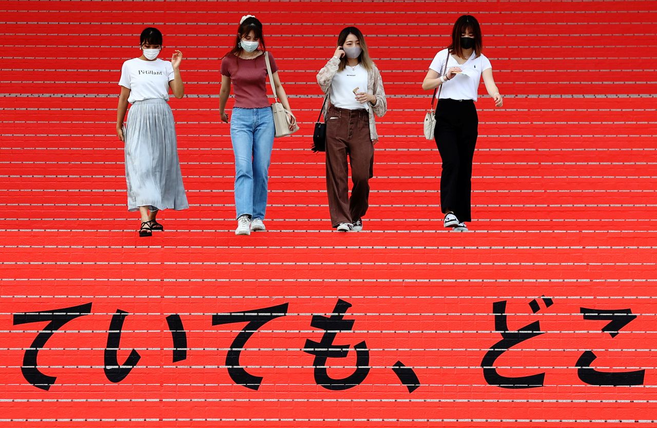 FILE PHOTO: Women wearing protective masks, amid the coronavirus disease (COVID-19) outbreak, walk on a stair bearing a slogan cheering Japanese team during Tokyo 2020 Olympic Games in Tokyo, Japan, August 7, 2021. REUTERS/Kim Kyung-Hoon