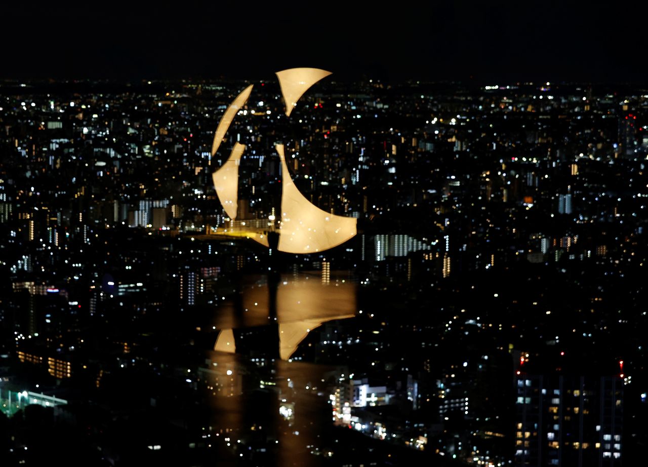 A visitor and moon-shaped light are reflected on a window at Sunshine City