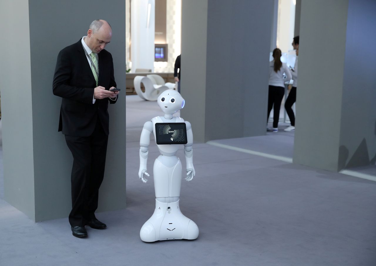 FILE PHOTO: A visitor looks at his mobile device next to Pepper the robot during the "Salon International de la Haute Horlogerie" (SIHH) watch fair in Geneva, Switzerland, January 14, 2019. REUTERS/Denis Balibouse/File Photo