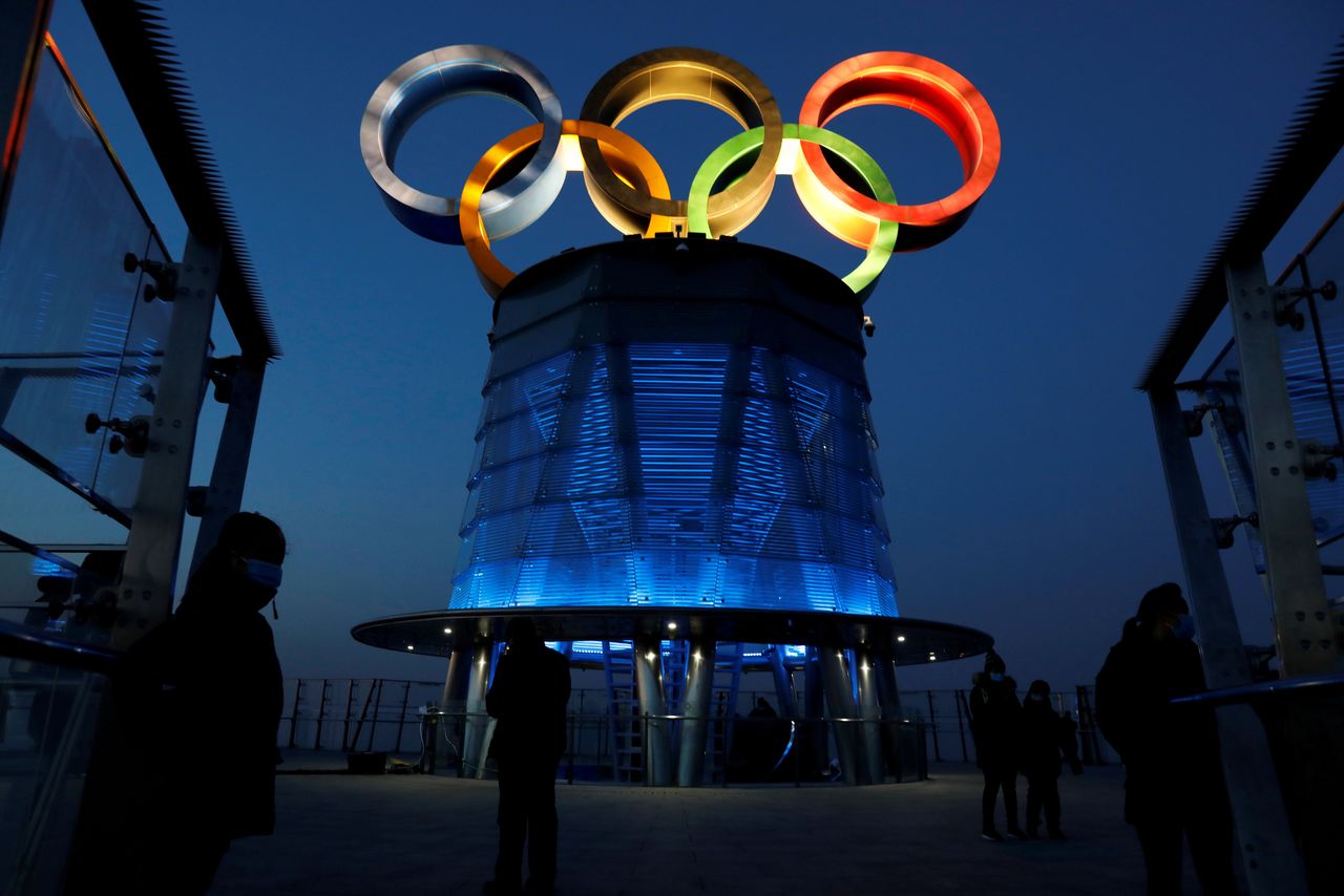 FILE PHOTO: People wearing face masks following the coronavirus disease (COVID-19) outbreak are seen near the lit-up Olympic rings at top of the Olympic Tower, a year ahead of the opening of the 2022 Winter Olympic Games, in Beijing, China February 4, 2021. REUTERS/Tingshu Wang