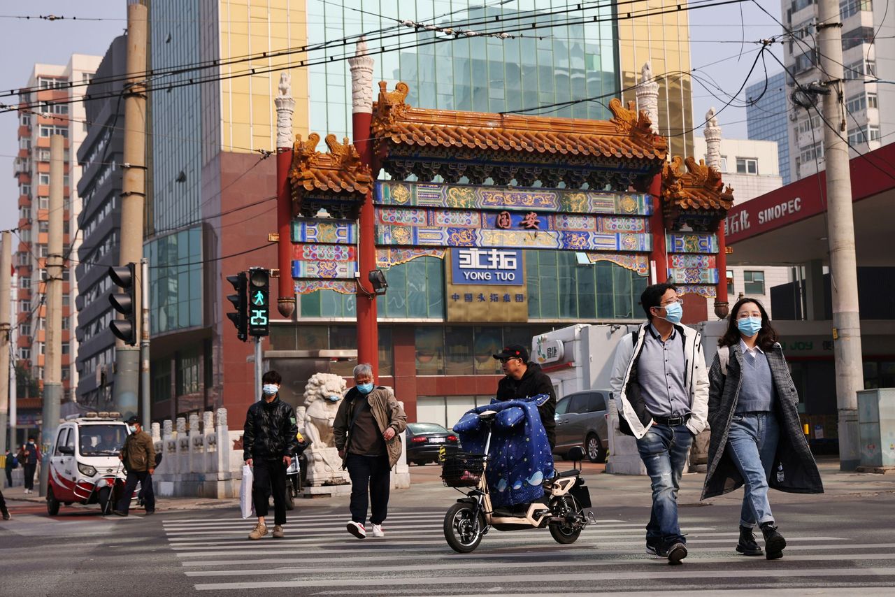 FILE PHOTO: People wearing face masks cross a street in Beijing, following outbreaks of the coronavirus disease (COVID-19) in China, October 25, 2021. REUTERS/Thomas Peter