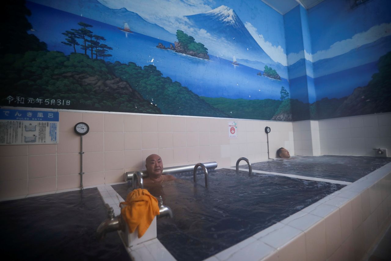 People soak in bathtubs with Mount Fuji painted on the walls at Japanese public bathhouse, or sento, 