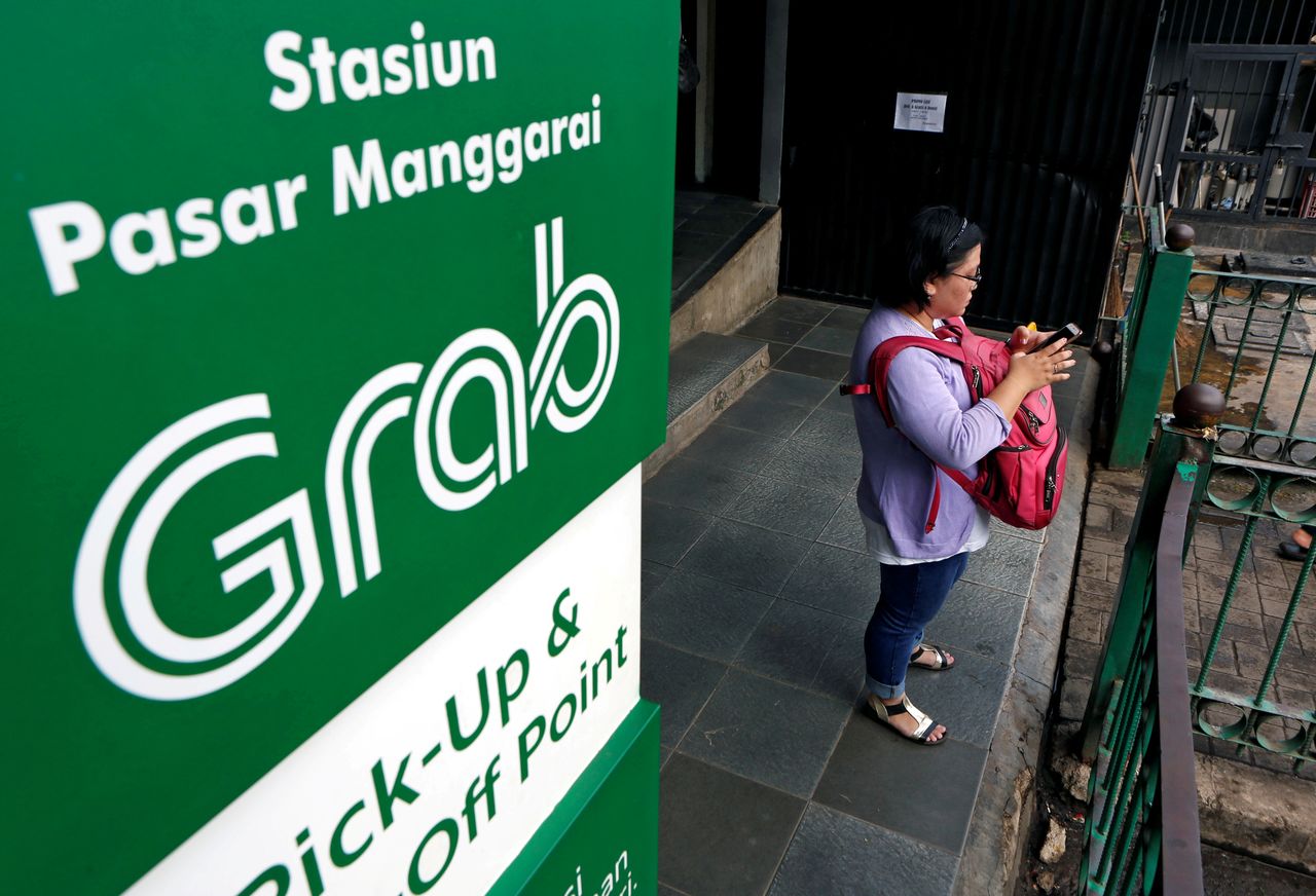 FILE PHOTO: A woman uses her phone near a sign for the online ride-hailing service Grab at the Manggarai train station in Jakarta, Indonesia July 3, 2017. REUTERS/Agoes Rudianto/File Photo