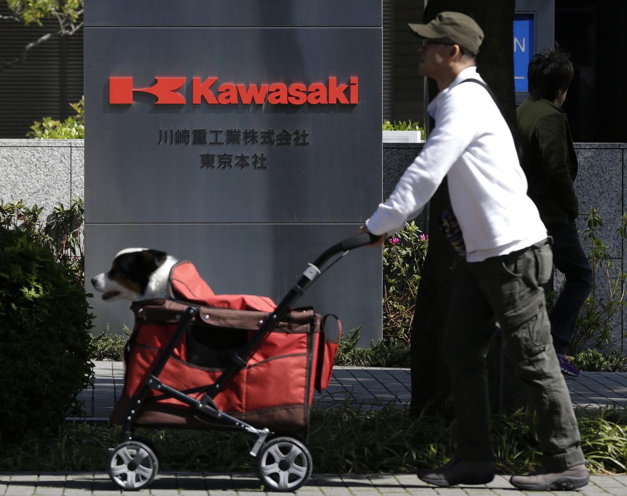FILE PHOTO: A man pushing his dog walks past a signboard of Kawasaki Heavy Industries, Ltd. at the company
