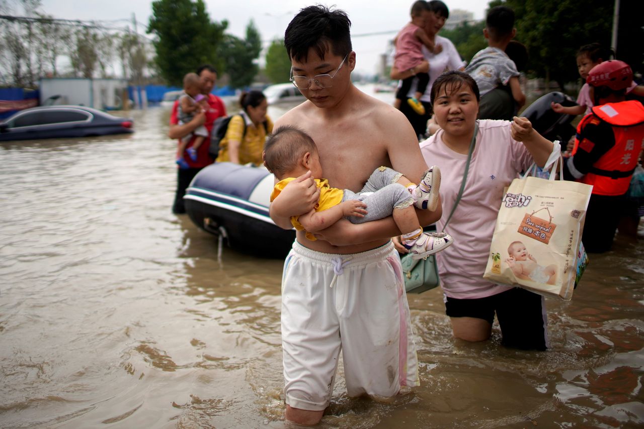 FILE PHOTO: A man holding a baby wades through a flooded road following heavy rainfall in Zhengzhou, Henan province, China July 22, 2021. REUTERS/Aly Song/File Photo