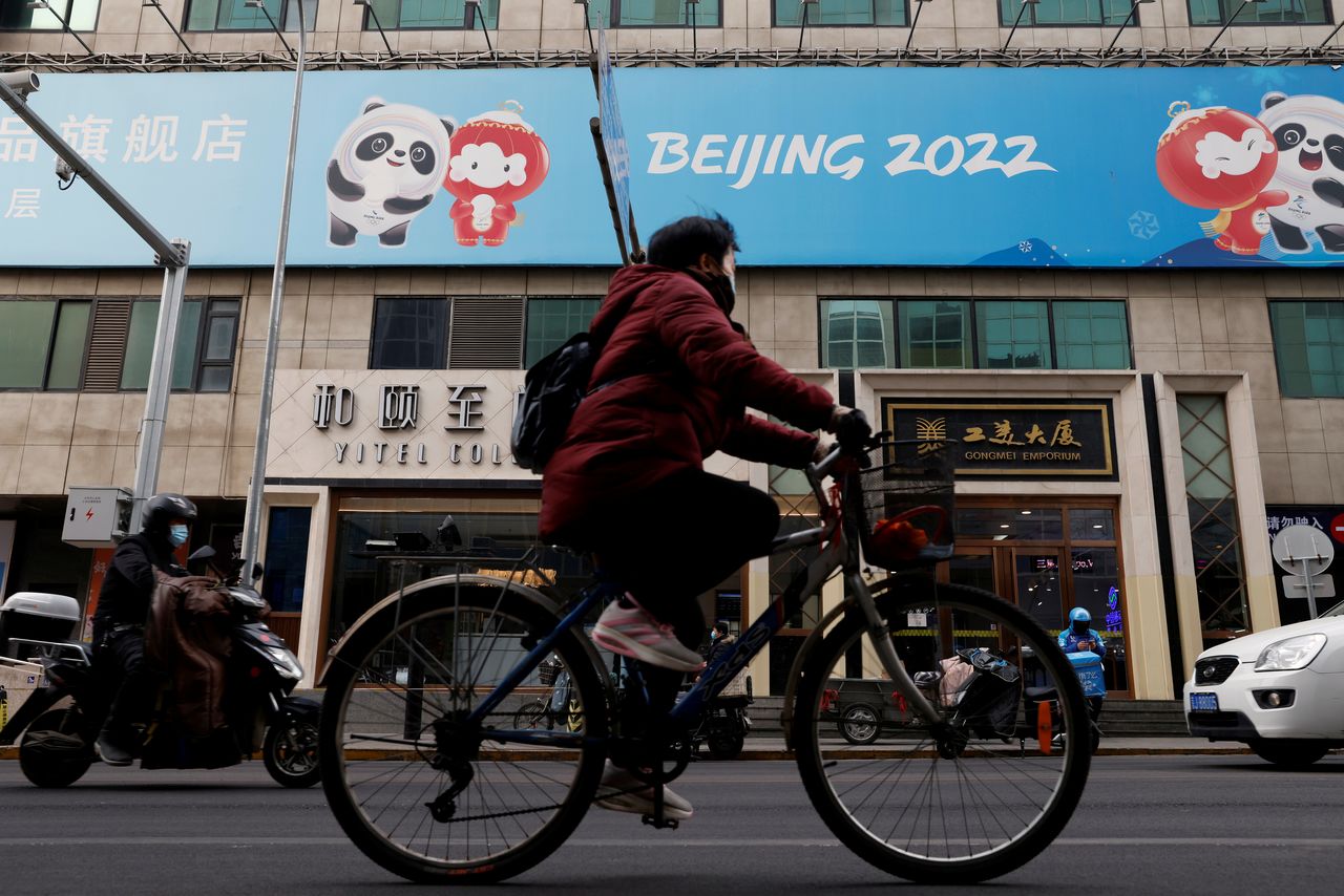 A man rides a bicycle past the sign of a flagship merchandise store for the Beijing 2022 Winter Olympics in Beijing, China December 8, 2021. REUTERS/Carlos Garcia Rawlins