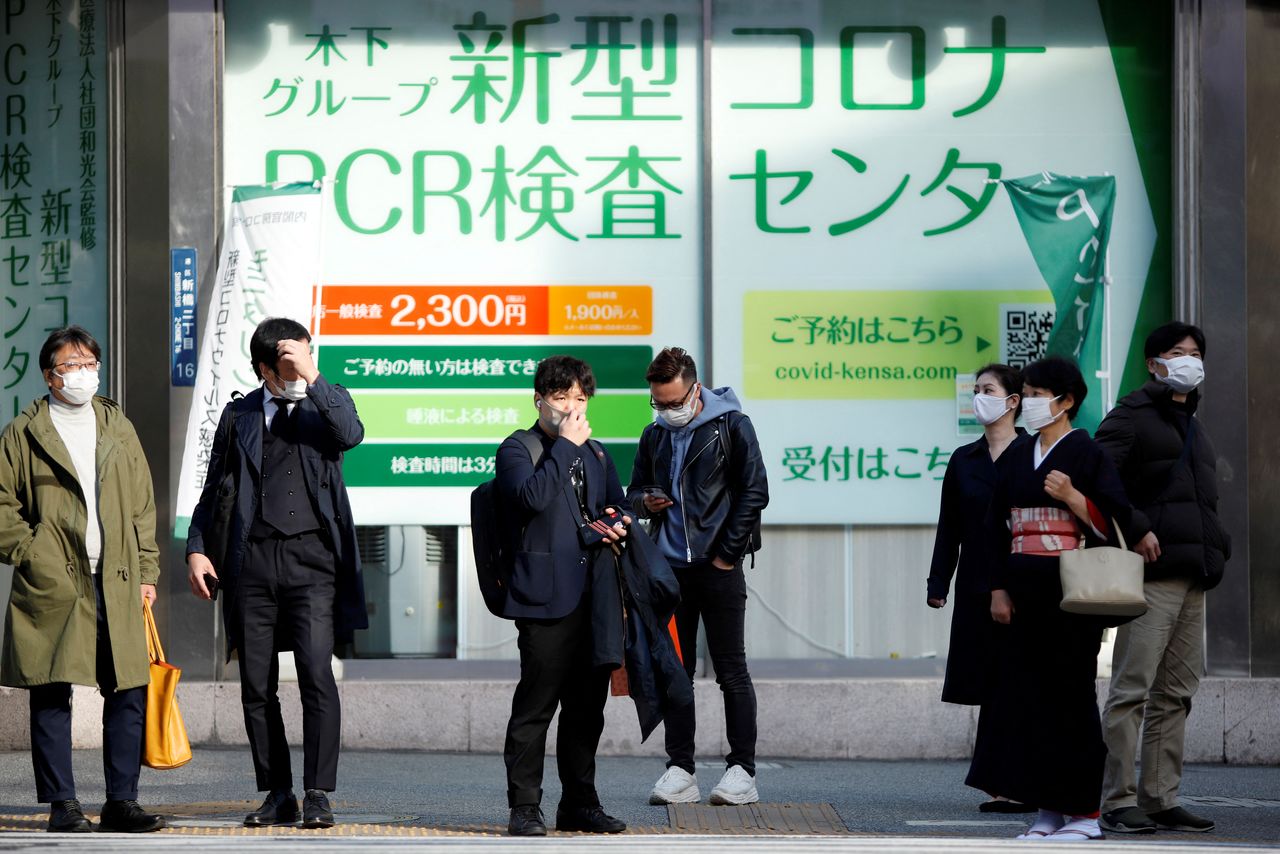 FILE PHOTO: People wait to cross the street in front of a PCR testing centre, on the first day of Japan