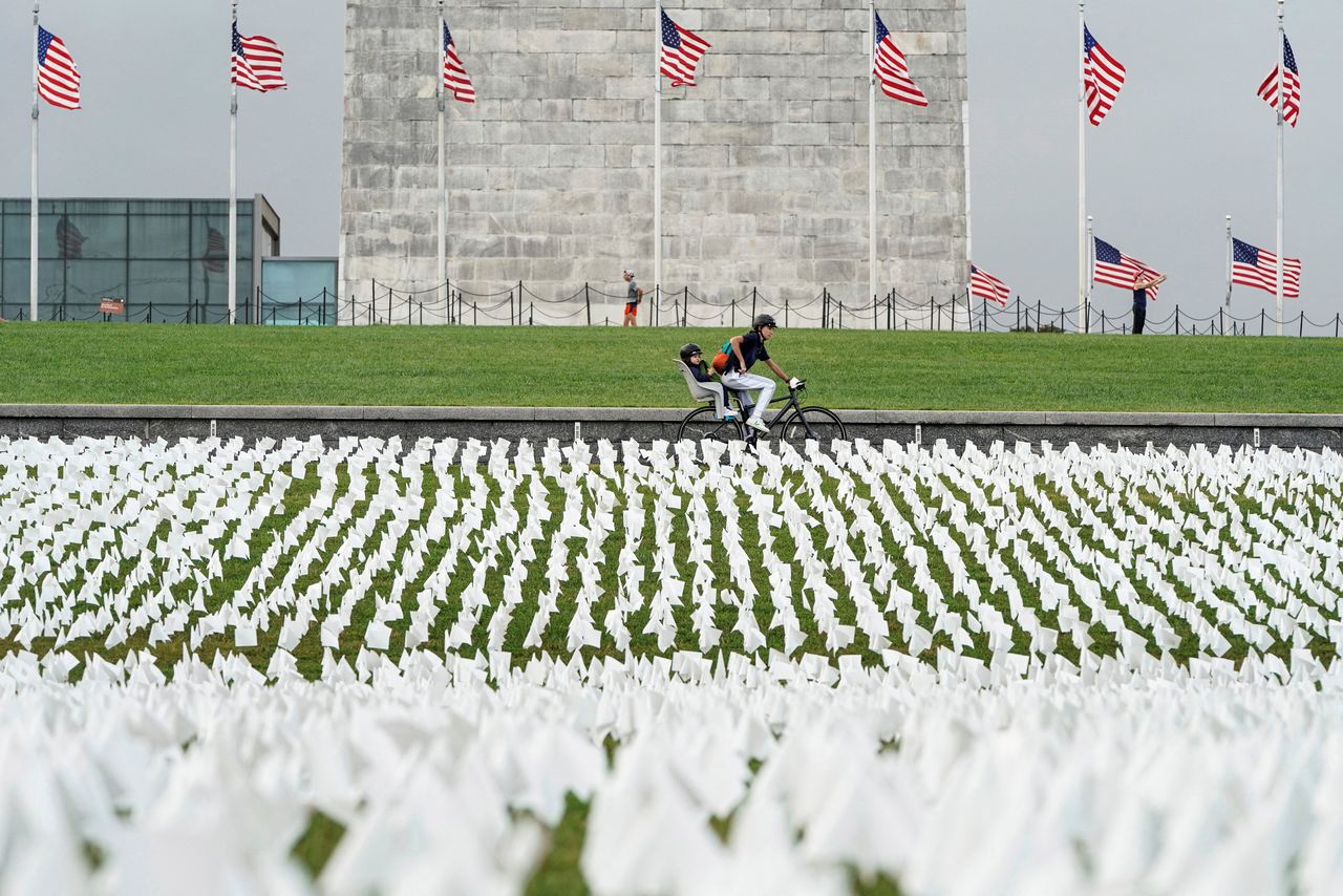 FILE PHOTO: A cyclist rides past an exhibition of white flags representing Americans who have died of coronavirus disease (COVID-19), placed over 20 acres of the National Mall, in Washington, U.S., September 17, 2021. REUTERS/Joshua Roberts