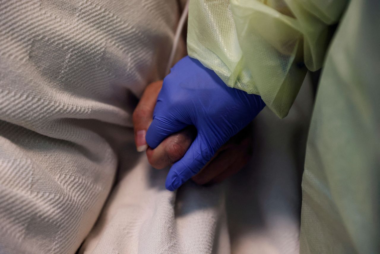 FILE PHOTO: A woman in her personal protective equipment (PPE) gear holds the hand of a coronavirus disease (COVID-19) positive patient, in her isolation room at Madison Memorial Hospital in Rexburg, Idaho, U.S., October 28, 2021. REUTERS/Shannon Stapleton