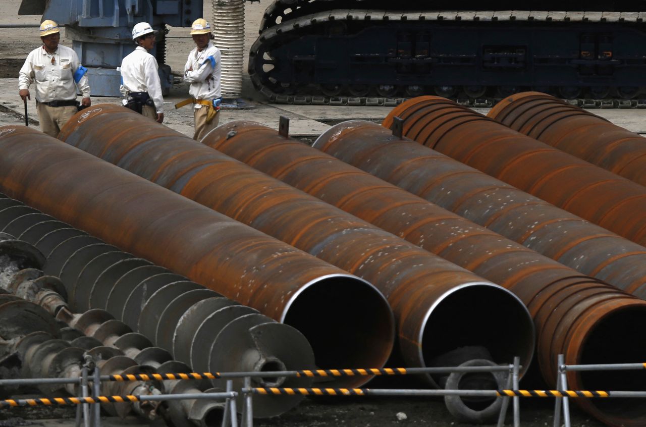 FILE PHOTO: Workers stand next to steel pipes at a construction site in Tokyo September 24, 2014. REUTERS/Yuya Shino