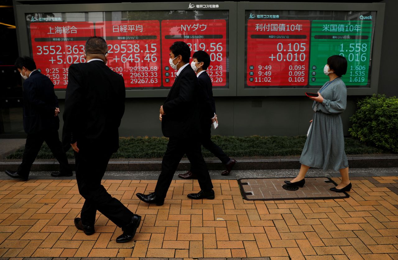 FILE PHOTO: Passersby wearing protective face masks walk past an electronic board displaying world stock indexes, amid the coronavirus disease (COVID-19) pandemic, in Tokyo, Japan November 1, 2021. REUTERS/Issei Kato