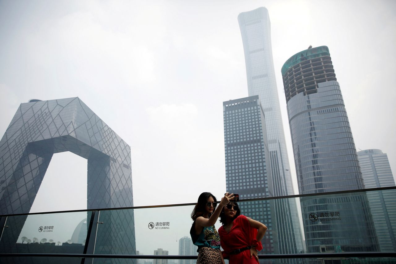 FILE PHOTO: Women pose for pictures at a shopping mall near the CCTV headquarters and China Zun skyscraper in Beijing