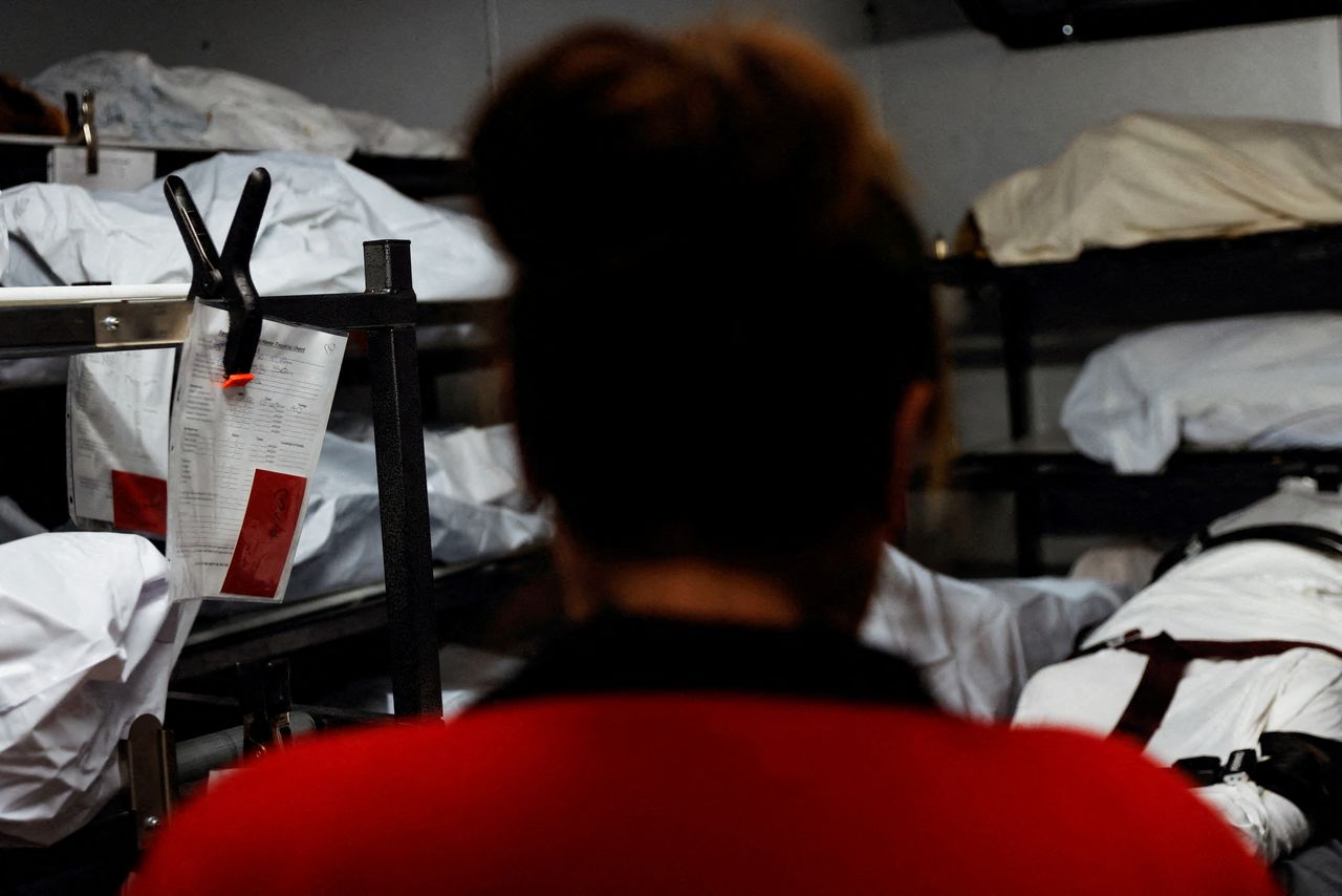 FILE PHOTO: Joanna Martinez, a funeral home worker, looks into a refrigeration cooler with decedents who passed on due to the coronavirus disease (COVID-19) marked with red tags inside a refrigeration cooler with other bodies not affected at the Farmington Funeral Home in Farmington, New Mexico, U.S., December 13, 2021. REUTERS/Shannon Stapleton