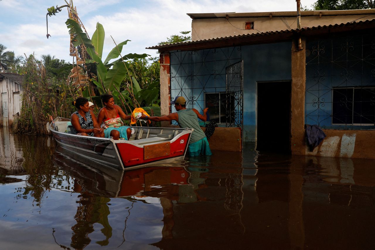 FILE PHOTO: Sergio da Silva dos Santos hands clothes to other residents in front of a flooded house accessed by canoe at Sambaituba in Ilheus, Bahia state, Brazil December 29, 2021. REUTERS/Amanda Perobelli/File Photo