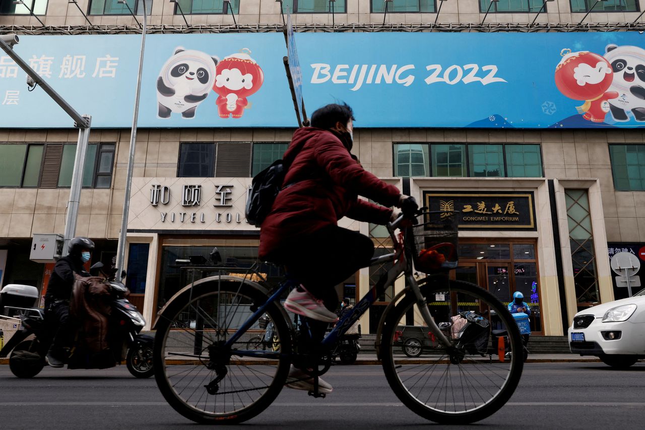 FILE PHOTO: A man rides a bicycle past the sign of a flagship merchandise store for the Beijing 2022 Winter Olympics in Beijing, China December 8, 2021. REUTERS/Carlos Garcia Rawlins