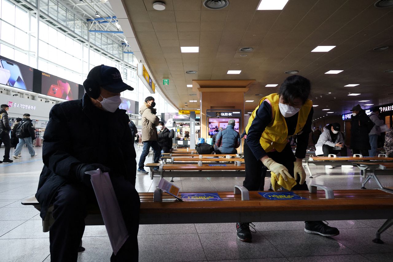 An employee disinfects a bench as a man wearing a mask to prevent contracting the coronavirus disease (COVID-19) looks on at a railway station in Seoul, South Korea, January 5, 2022.   REUTERS/Kim Hong-Ji