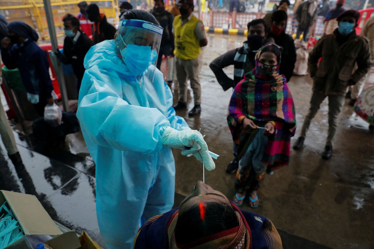 A healthcare worker collects a coronavirus disease (COVID-19) test swab sample from a woman as others wait, amidst the spread of the disease, at a railway station in New Delhi, India, January 5, 2022. REUTERS/Adnan Abidi