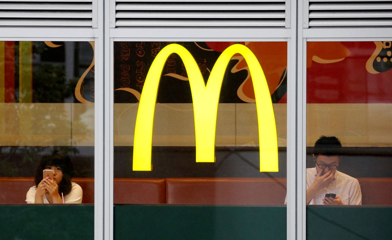 FILE PHOTO: Customers using mobile phones, are seen through the windows of a McDonald