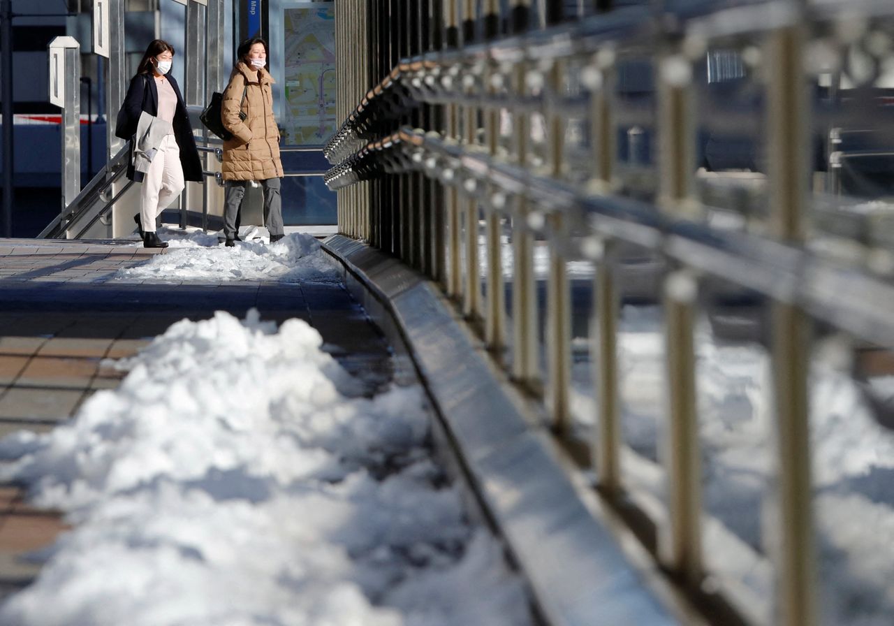 FILE PHOTO: Passengers wearing protective face masks walk next to lingering snow on the street, amid the coronavirus disease (COVID-19) pandemic, in Tokyo, Japan, January 7, 2022. REUTERS/Issei Kato