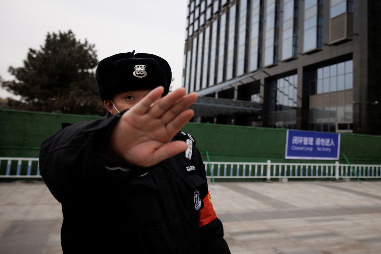 A security guard attempts to prevent the photographer from taking pictures outside a fence surrounding a hotel inside a closed loop area, created to prevent the spread of the coronavirus disease (COVID-19) at the Beijing 2022 Winter Olympics, in Beijing, China, January 12, 2022. REUTERS/Thomas Peter