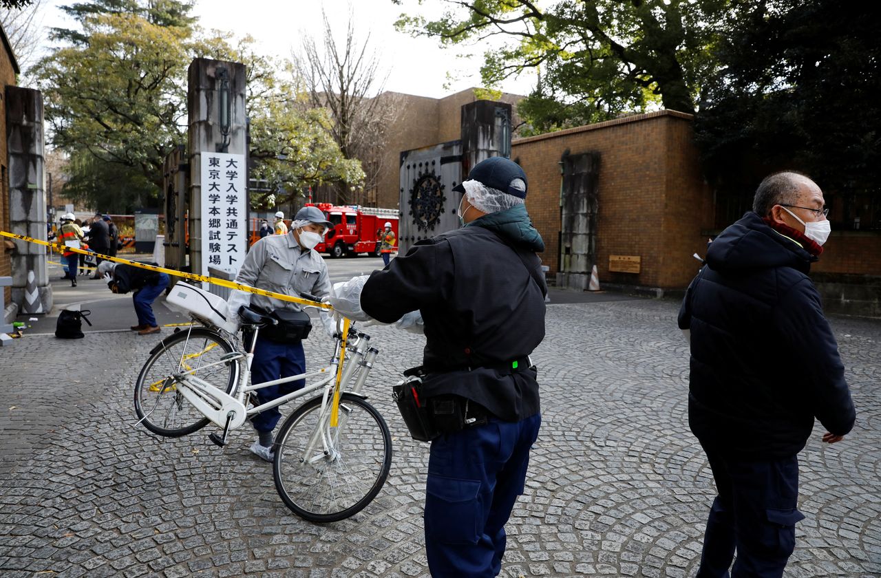 A man moves a bicycle as police officers inspect the site where a stabbing incident happened at an entrance gate of Tokyo University in Tokyo, Japan January 15, 2022. REUTERS/Issei Kato