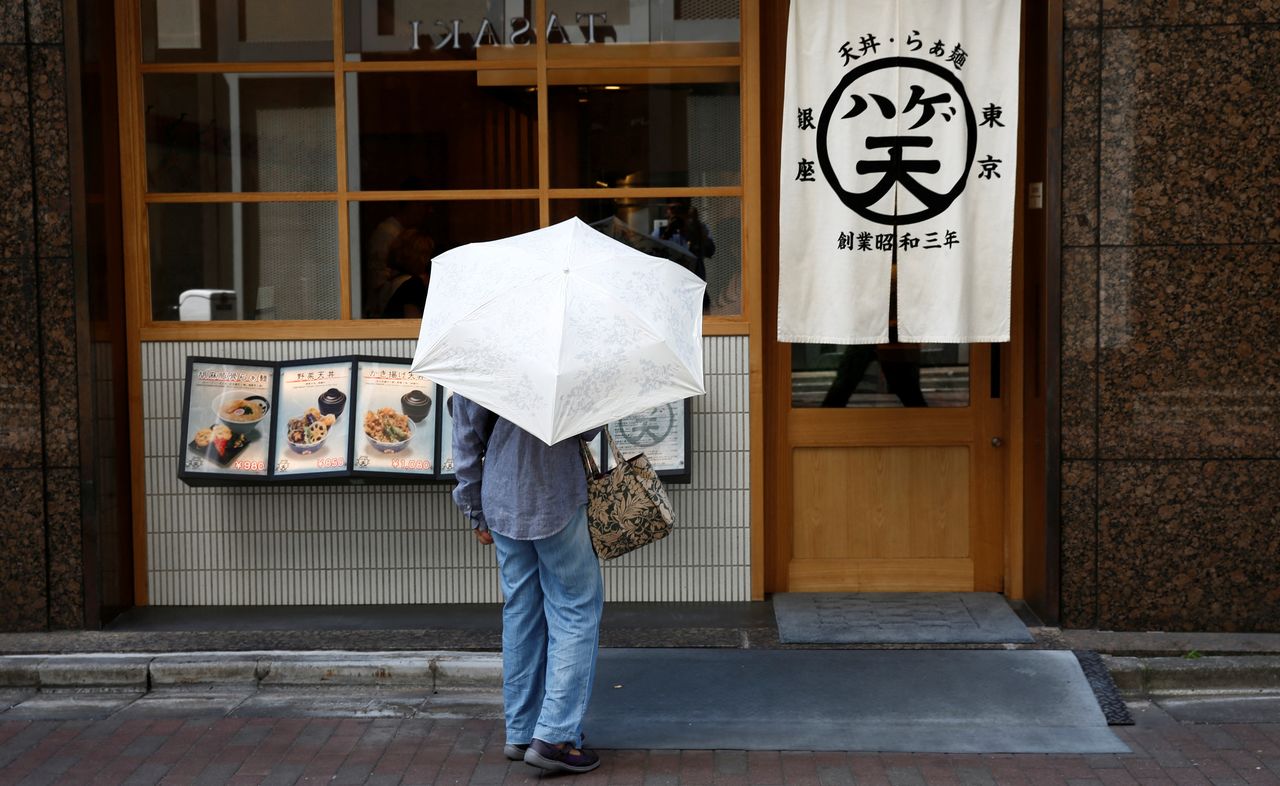 FILE PHOTO: A woman holding a parasol looks at a menu board in front of a restaurant at a shopping district in Tokyo, Japan, July 20, 2018.  REUTERS/Kim Kyung-Hoon