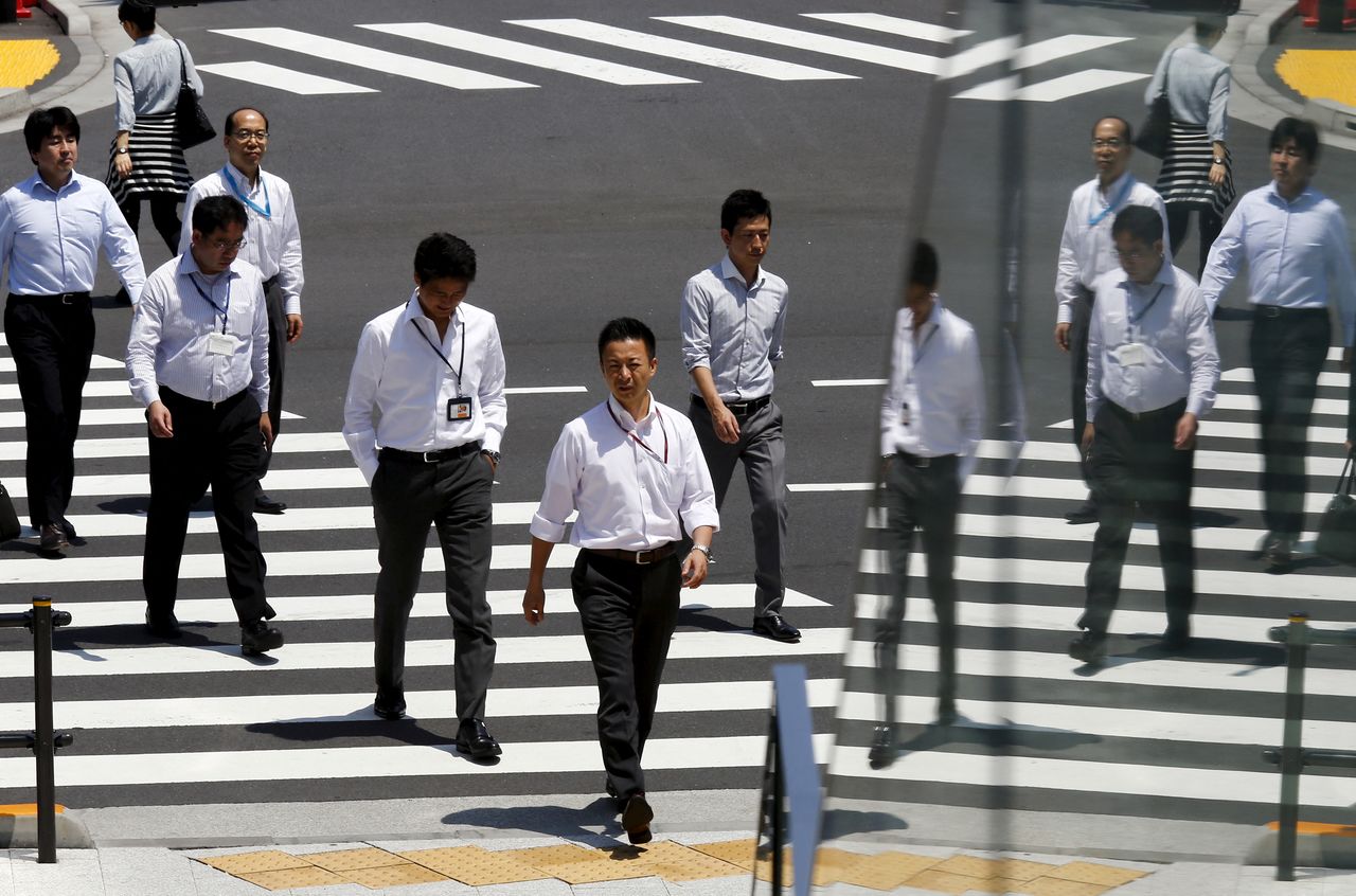 FILE PHOTO: Office workers are reflected in a glass railing as they cross a street during lunch hour in Tokyo June 1, 2015.  REUTERS/Thomas Peter