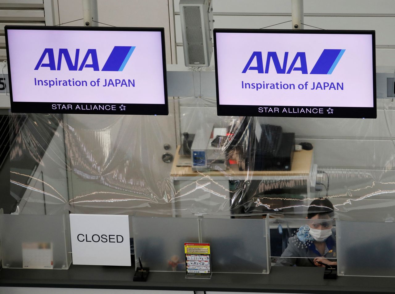 FILE PHOTO: A staff member of All Nippon Airways (ANA) wearing a protective face mask sits behind a plastic curtain, installed in order to prevent infections following the coronavirus disease (COVID-19) outbreak, at a counter in a terminal of the Tokyo International Airport, Tokyo Japan October 27, 2020. REUTERS/Kim Kyung-Hoon