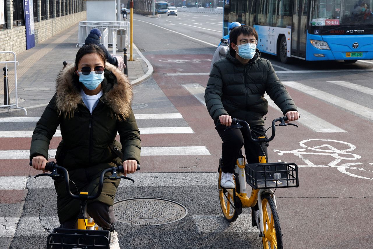 FILE PHOTO: People wearing protective masks ride bicycles, as the coronavirus disease (COVID-19) pandemic continues, in Beijing, China January 30, 2022. REUTERS/Tyrone Siu