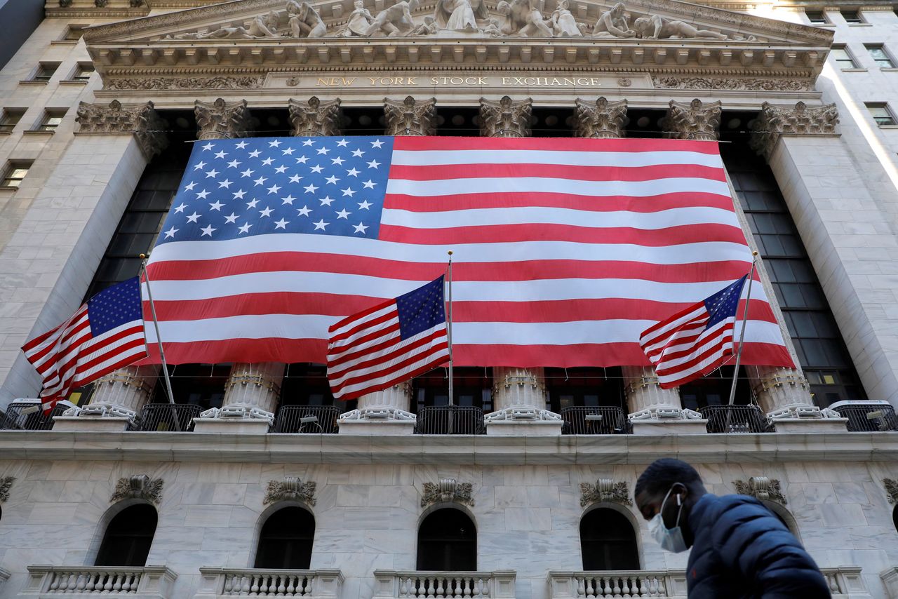 FILE PHOTO: A man in a surgical mask walks by the New York Stock Exchange (NYSE) as coronavirus continued to influence markets in Manhattan, New York City, New York, U.S., March 16, 2020. REUTERS/Andrew Kelly/File Photo