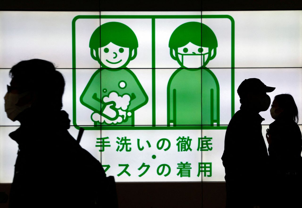 Passersby wearing protective face masks walk past in front of an electric screen displaying notice about COVID-19 safety measures, amid the coronavirus disease (COVID-19) pandemic, in Tokyo, Japan, February 1, 2022. REUTERS/Issei Kato