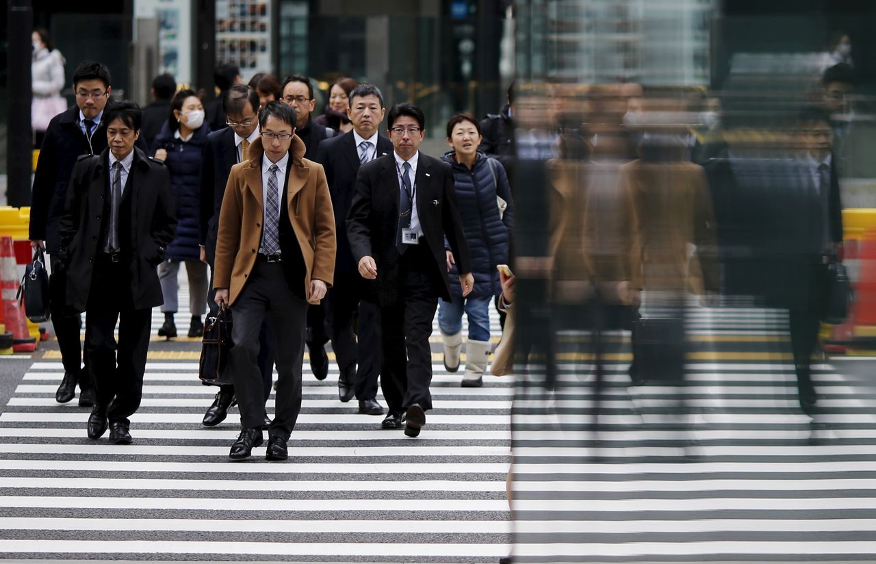FILE PHOTO: People are reflected on a wall as they cross a road at Tokyo