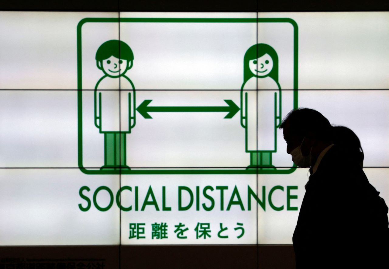 FILE PHOTO: Passersby wearing protective face masks walk past in front of an electric screen displaying notice about COVID-19 safety measures, amid the coronavirus disease (COVID-19) pandemic, in Tokyo, Japan, February 1, 2022. REUTERS/Issei Kato