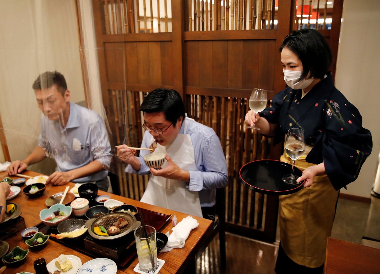 FILE PHOTO: A waitress serves Japanese sake to customers during dinner at Japanese restaurant Kazu, on the first day after Japan lifted the state of emergency imposed due to the coronavirus disease (COVID-19) outbreak, in Tokyo, Japan, October 1, 2021. REUTERS/Kim Kyung-Hoon