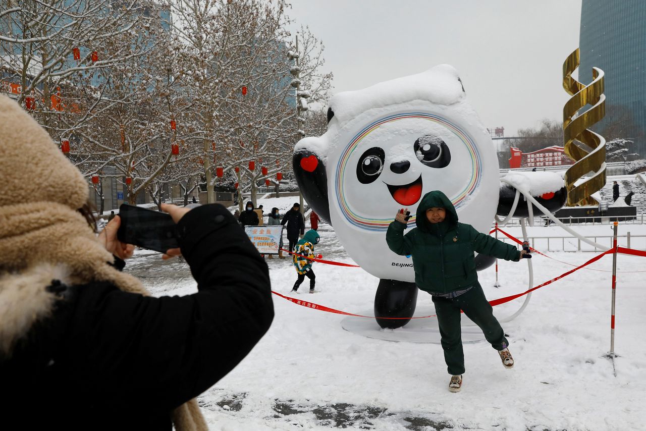 A person poses for pictures in front of an installation featuring Bing Dwen Dwen, the Beijing 2022 Winter Olympic Mascot amidst a snowfall on a street in Beijing, China February 13, 2022. REUTERS/Tingshu Wang