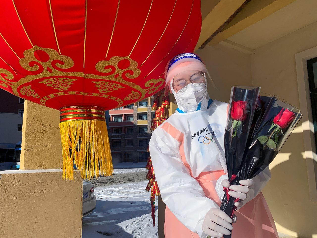 Beijing 2022 Winter Olympics volunteer Stella poses with single red roses as she hands them out to journalists and personnel leaving a 