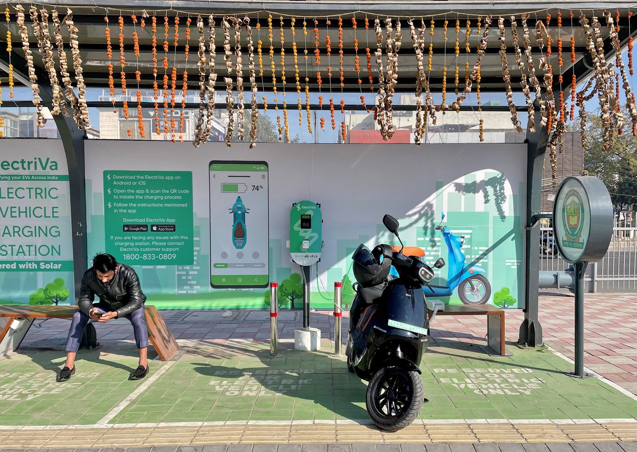 A man checks his mobile phone as he waits while recharging his Ola electric scooter at an electric vehicle charging station in New Delhi, India, February 12, 2022. REUTERS/Aditi Shah