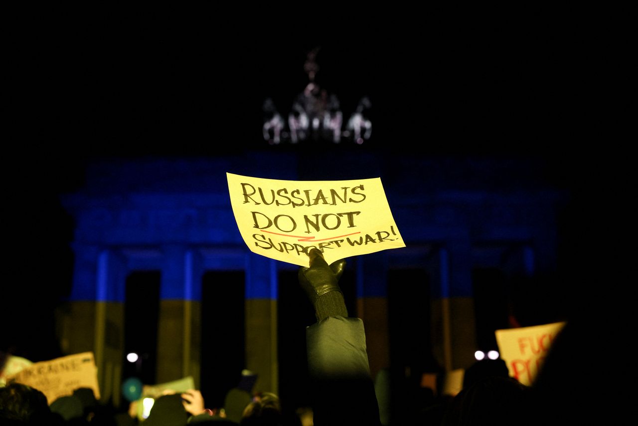 A person holds a sign in front of Brandenburg Gate lit up in the colours of Ukrainian flag during an anti-war protest, after Russia launched a massive military operation against Ukraine, in Berlin, Germany February 24, 2022. REUTERS/Christian Mang
