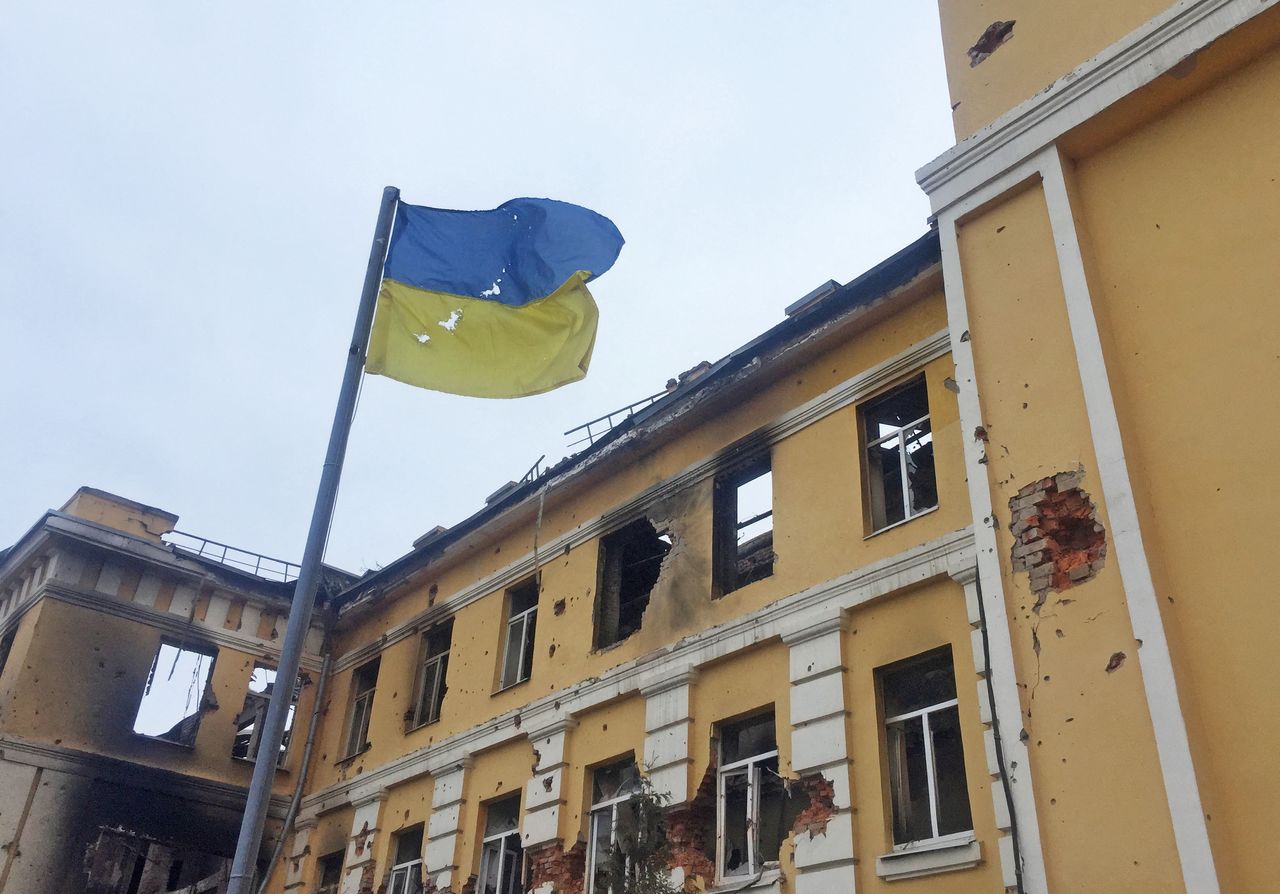 The Ukrainian national flag is seen in front of a school which, according to local residents, was on fire after shelling, as Russia
