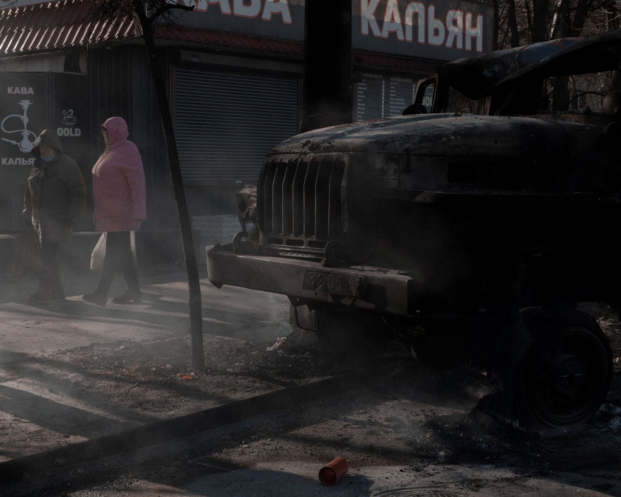 People walk past a burnt vehicle, as Russia