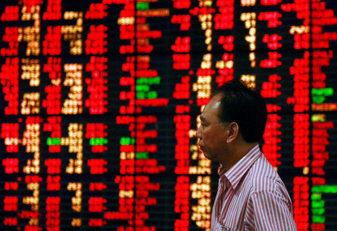 FILE PHOTO: A Thai investor walks past an electronic board displaying live market data at a stock broker