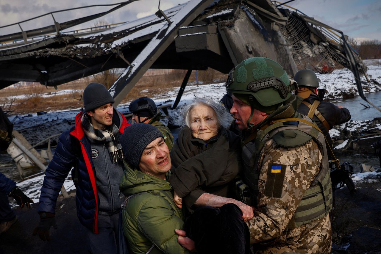 Two men carry a woman as people flee from advancing Russian troops whose attack on Ukraine continues in the town of Irpin outside Kyiv, Ukraine, March 8, 2022. REUTERS/Thomas Peter