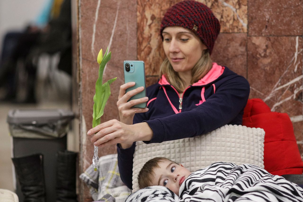 Daniel tries to rest in his mothers lap as she takes a picture of a tulip received from a volunteer, on a mattress laid inside the ticket office at the North Railway Station, after having fled Ukraine following the Russian invasion, in Bucharest, Romania, March 8, 2022. Inquam Photos/Octav Ganeavia REUTERS