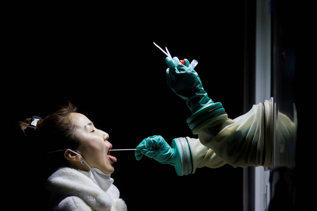 FILE PHOTO: A woman receives a throat swab test at a street booth as the coronavirus disease (COVID-19) pandemic continues in Beijing, China, January 17, 2022. REUTERS/Thomas Peter