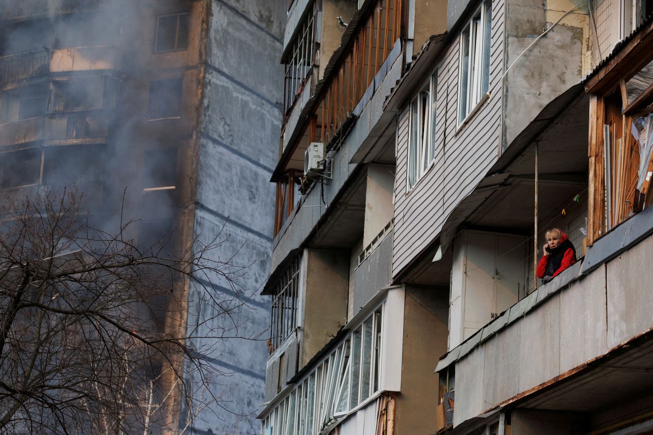 A woman stands in a balcony next to a residential building that was hit by shelling as Russia