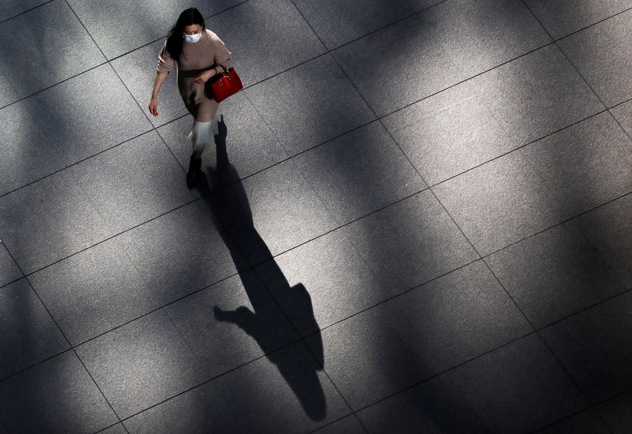 FILE PHOTO: A woman wearing a protective face mask walks inside a buildng at a business district, amid the coronavirus disease (COVID-19) outbreak, in Tokyo, Japan November 18, 2020.  REUTERS/Issei Kato