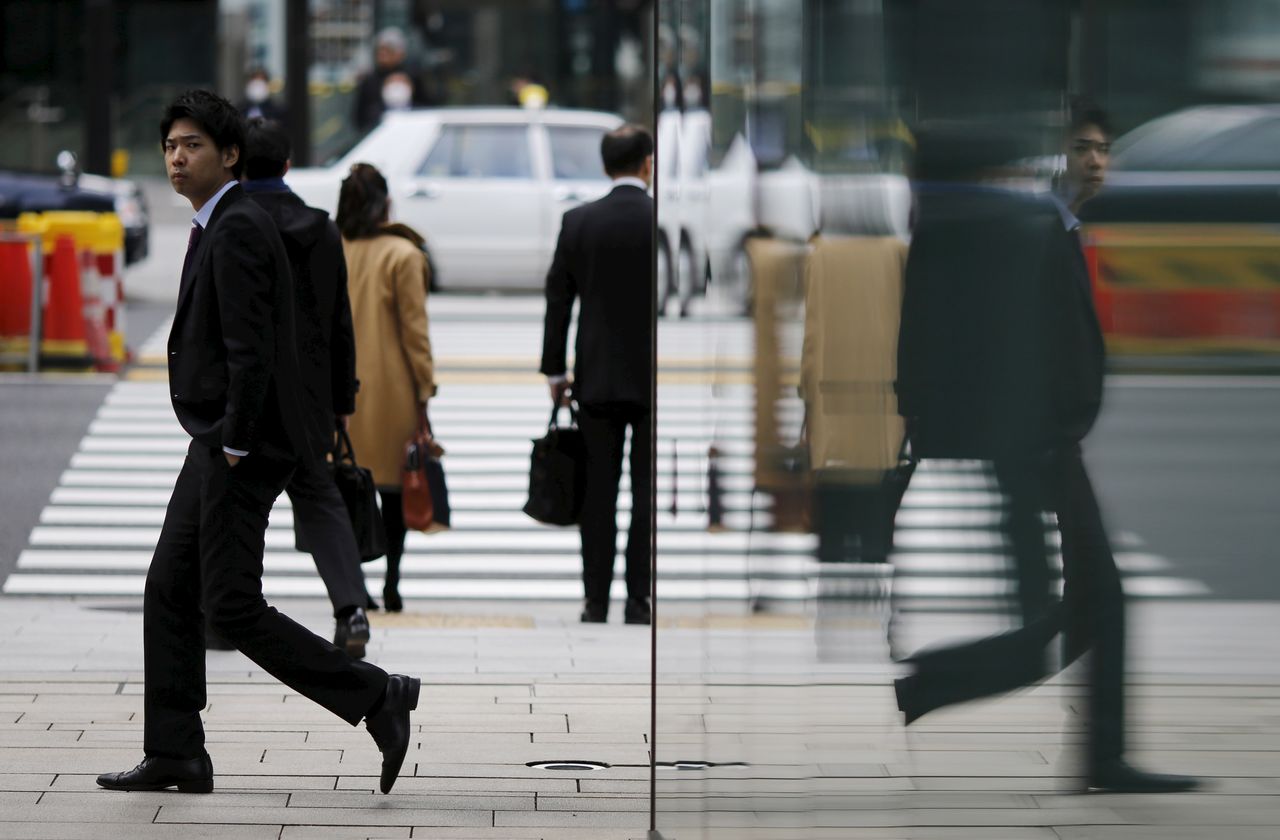 FILE PHOTO: A businessman is reflected on a wall as he walks along Tokyo