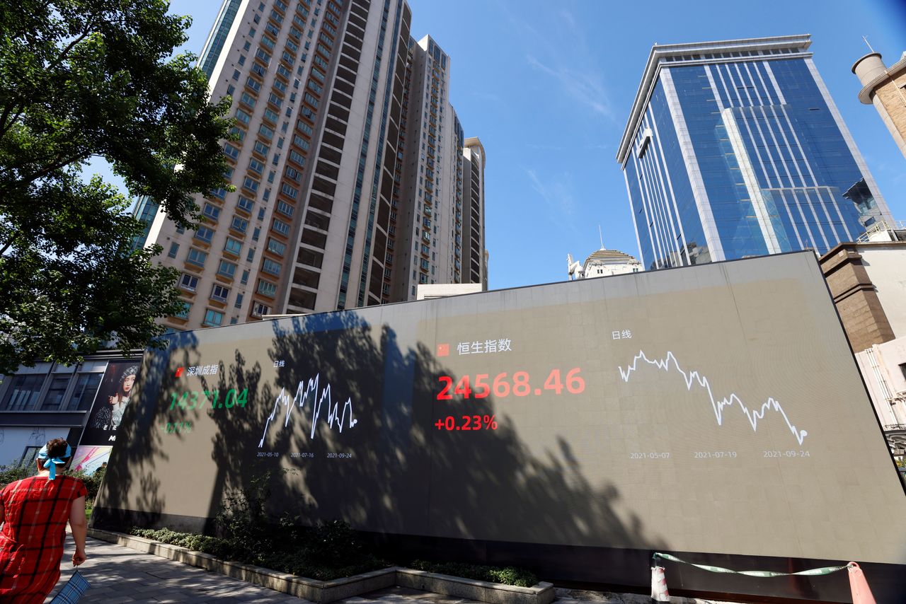 FILE PHOTO: A woman walks by an electronic display showing the Shenzhen and Hang Seng stock indexes, in Shanghai, China, September 24, 2021. REUTERS/Aly Song