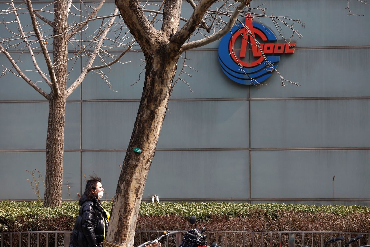 A woman wearing a face mask walks past a sign of China National Offshore Oil Corp (CNOOC) outside its headquarters in Beijing, China March 8, 2021. REUTERS/Tingshu Wang